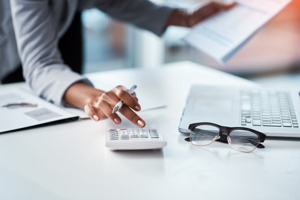 Accountant, businesswoman or banker using calculator, checking paperwork and documents while preparing financial data report in an office. Hands of a woman doing payroll or calculating annual tax.